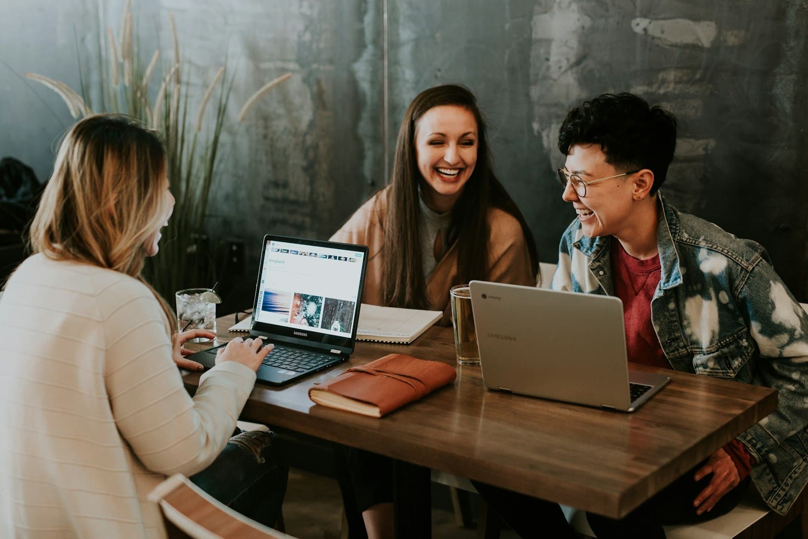 Three young people laughing together around their laptops at a table