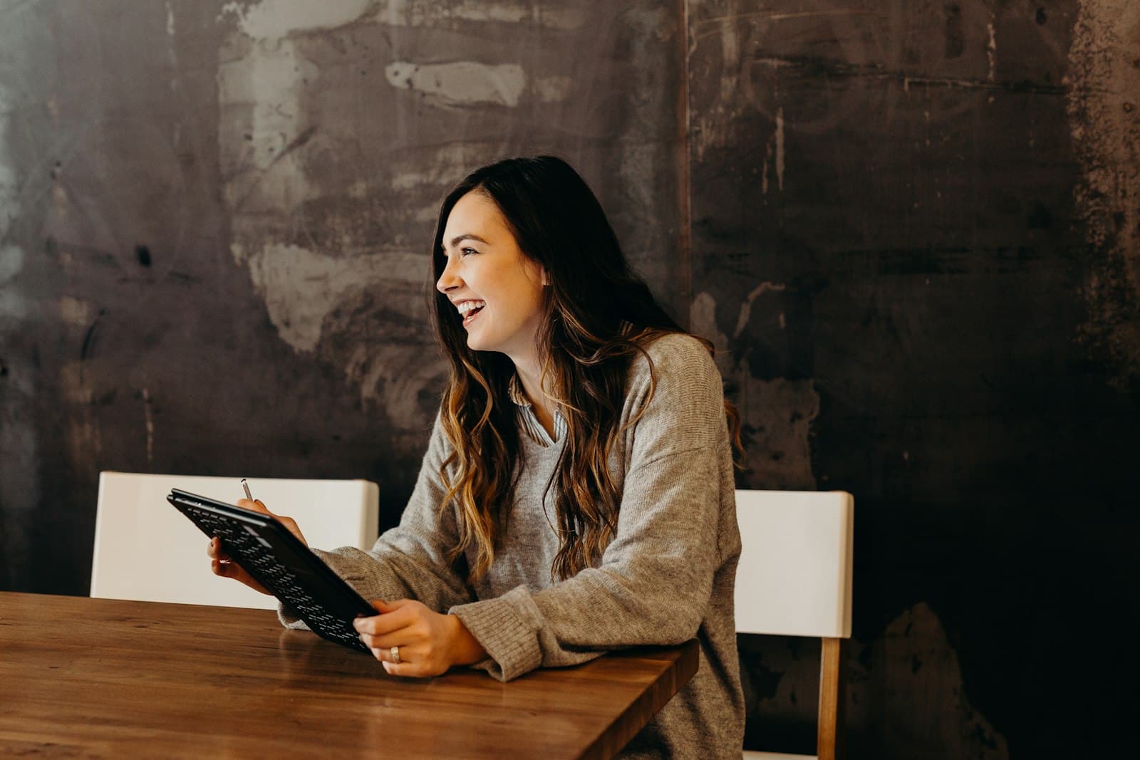 A young woman smiling as she works on a tablet at a wooden table