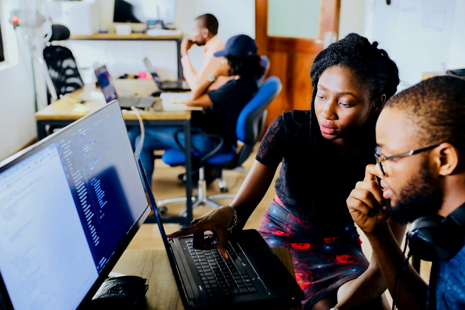 One developer points at code on a laptop while another listens