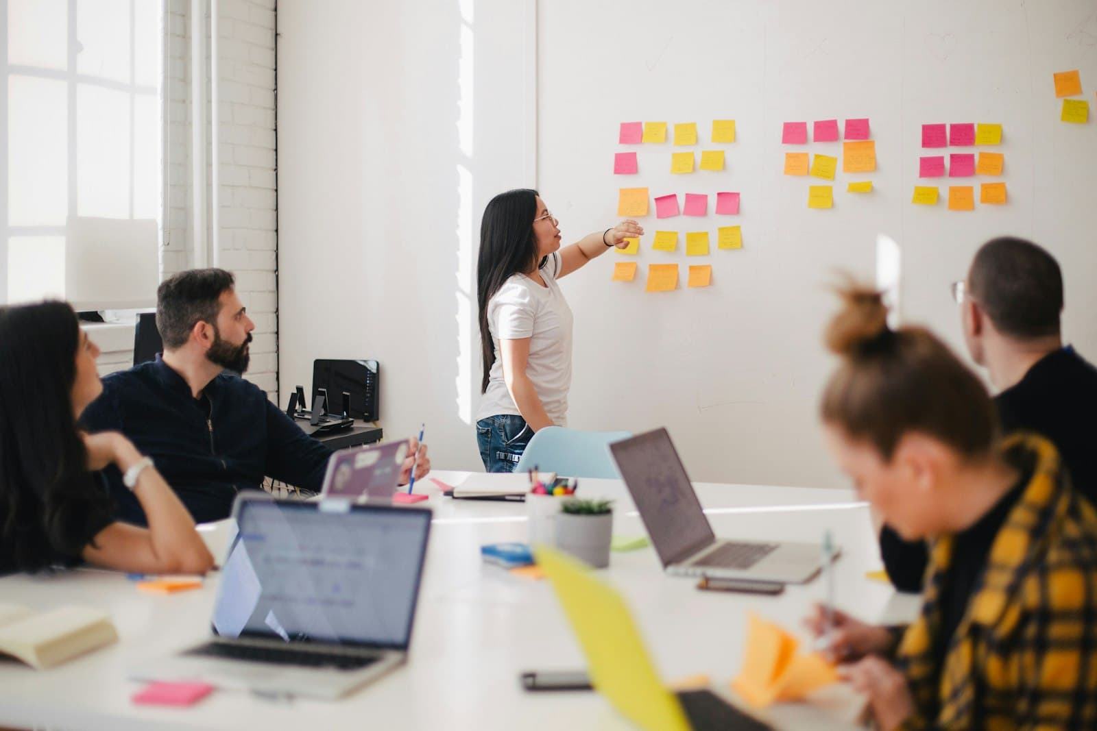 A team meeting in a bright office, one person pointing at sticky notes on the wall